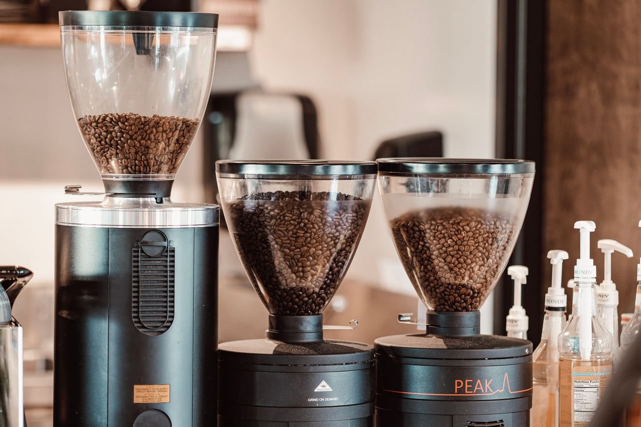 services-bg Close-up of coffee grinders filled with roasted beans in a modern cafe setting.