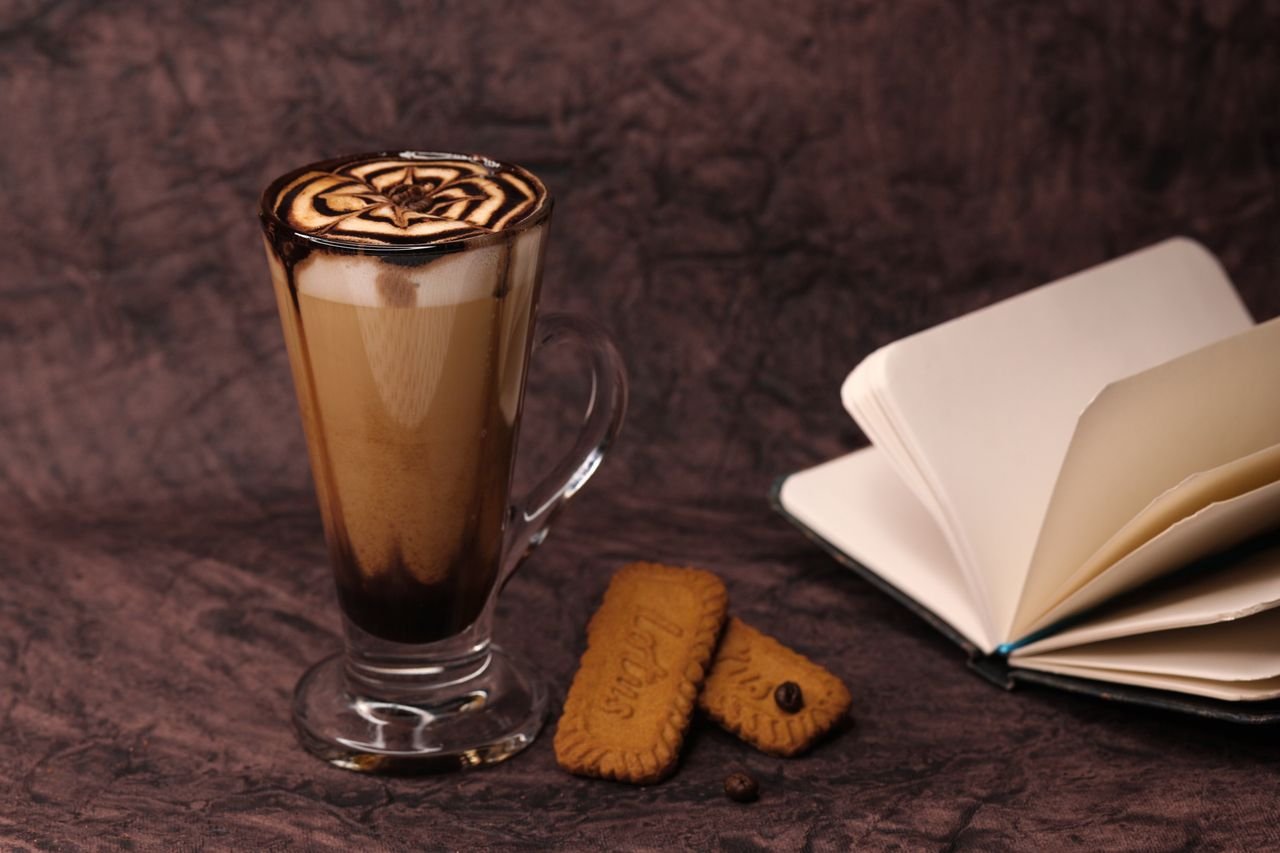 Aesthetic shot of a latte in a tall glass with cookies and an open notebook.