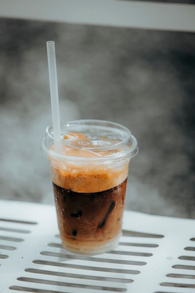 Cold iced coffee with cream in a clear plastic cup on a metal bench, perfect for summer refreshment.