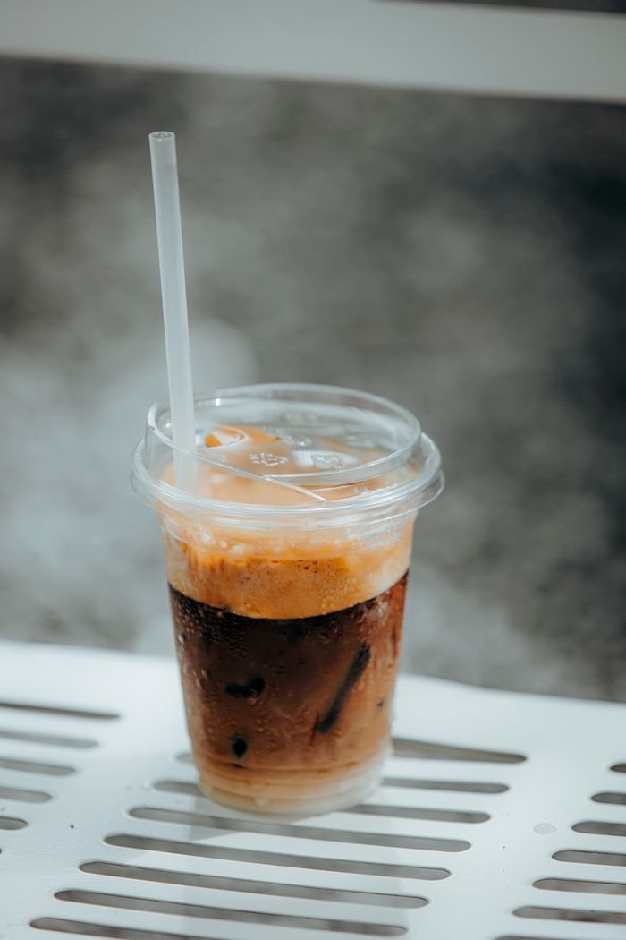 services-03 Cold iced coffee with cream in a clear plastic cup on a metal bench, perfect for summer refreshment.